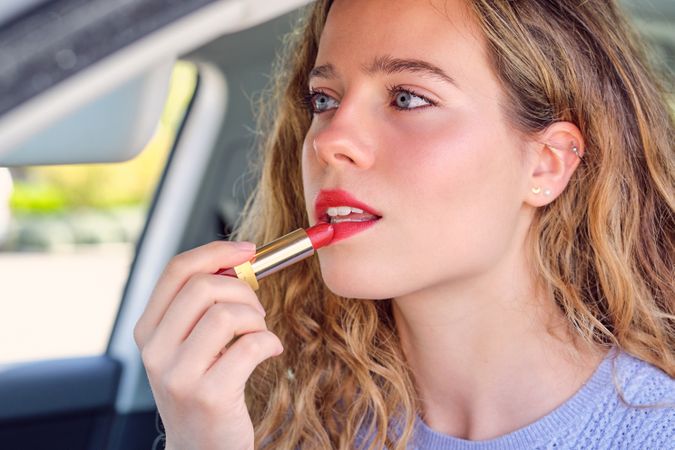 Crop gorgeous woman applying red lipstick in car