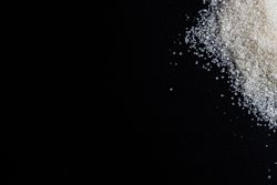 Flat lay of granulated sugar positioned on the right side over a dark background.