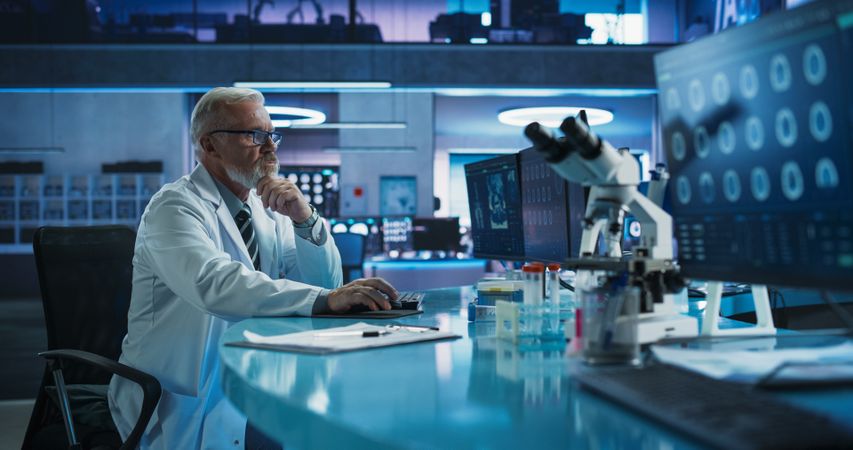 Male Neuroscientist Using Desktop Computer To Analyze MRI Scans Of Brain In Medical Research Center Laboratory.