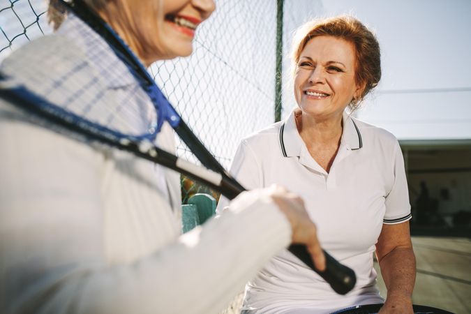 Mature women sitting on a bench near a tennis court and talking
