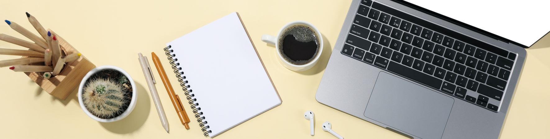 Top view banner of laptop, notebook, pens, coffee, cactus, earbuds with copy space