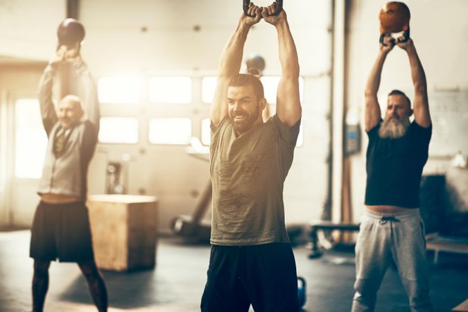 Group of happy people in fitness class with kettlebells overhead