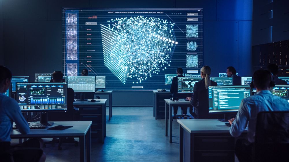 In a Modern Control Center, a Diverse Team Analyzes Data on Multiple Screens, Focusing on a Large Digital Display With Intricate Neural Network Visuals for Strategic Insights.
