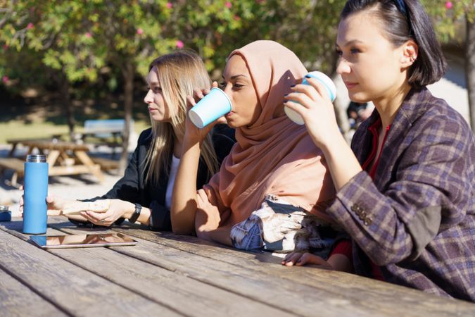 Female friends sipping coffee from to go cups and looking ahead