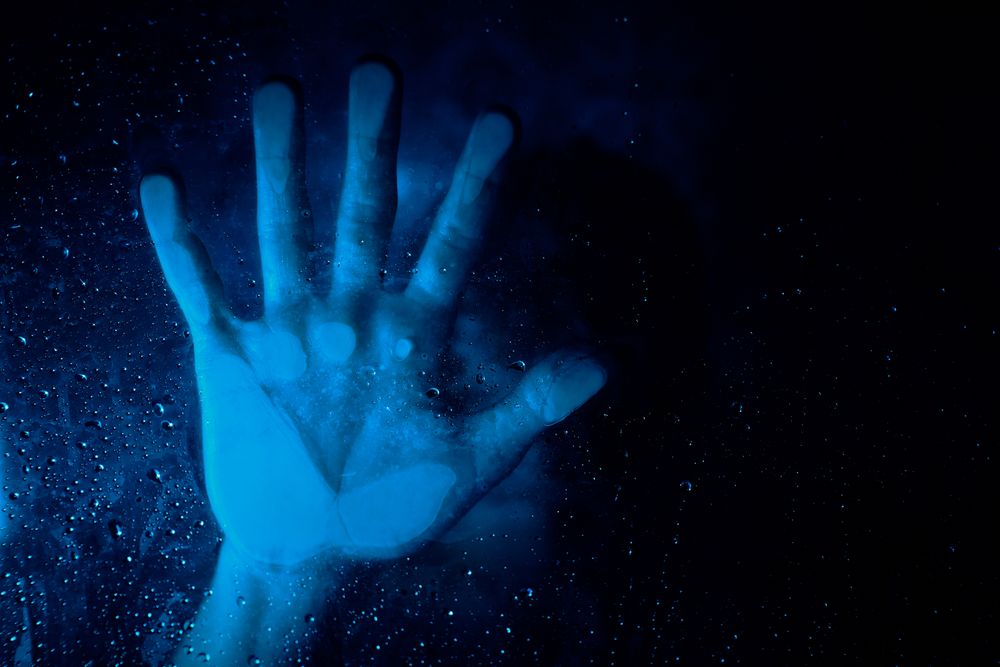 Anonymous hopeless person behind wet glass wall in neon light