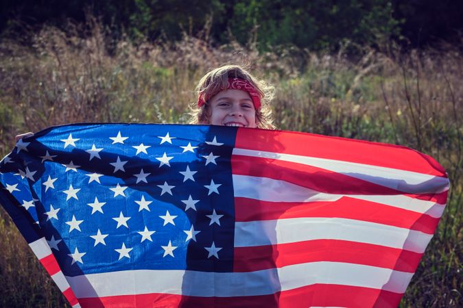 Smiling preteen boy stretching flag of USA in hands