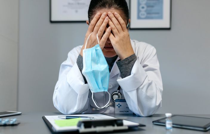Female doctor with pandemic fatigue covering her face