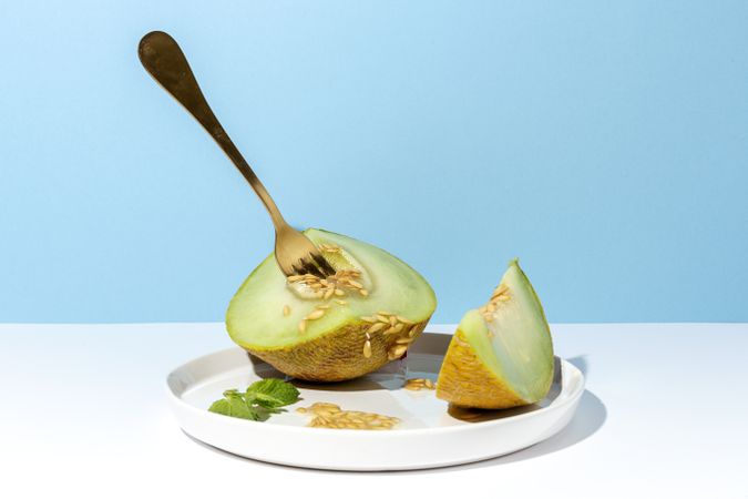 Sliced small melon on plate with spoon and fork