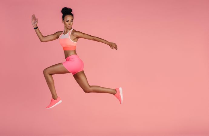 Woman in sportswear running over pink background