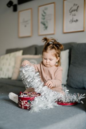 Girl playing with Christmas decoration sitting on couch