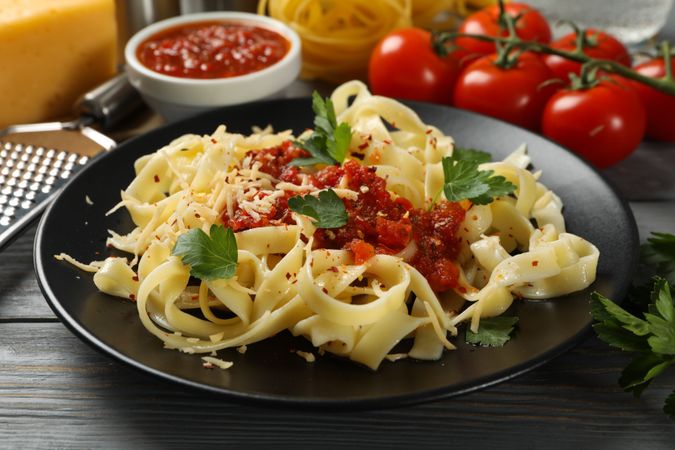 Composition with plate of tasty pasta and ingredients for cooking on wooden background