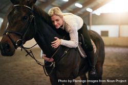Horse owner sitting astride and lovingly hugging her brown horse 56Pqzb