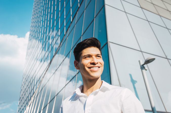 Smiling young man in sunlight under skyscraper
