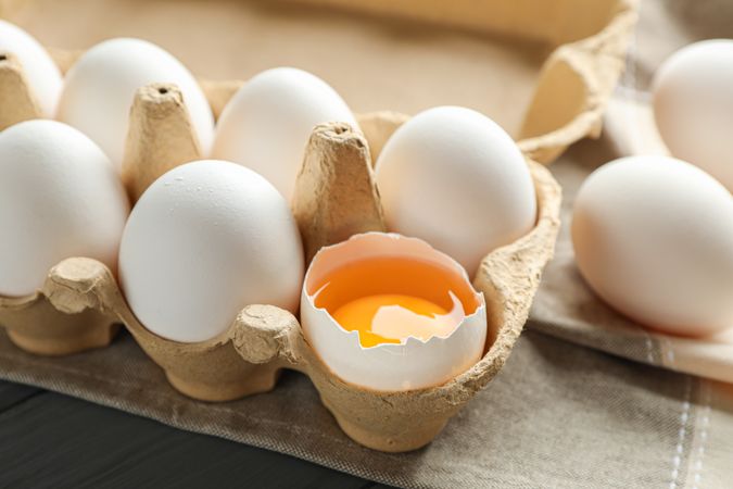 chicken eggs in carton box and kitchen towel on wooden table, space for text and closeup