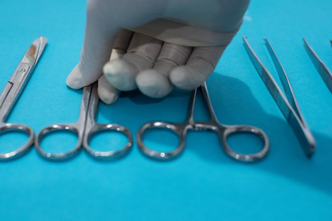 Hand doctor taking scissors or forceps surgical instrument on blue background