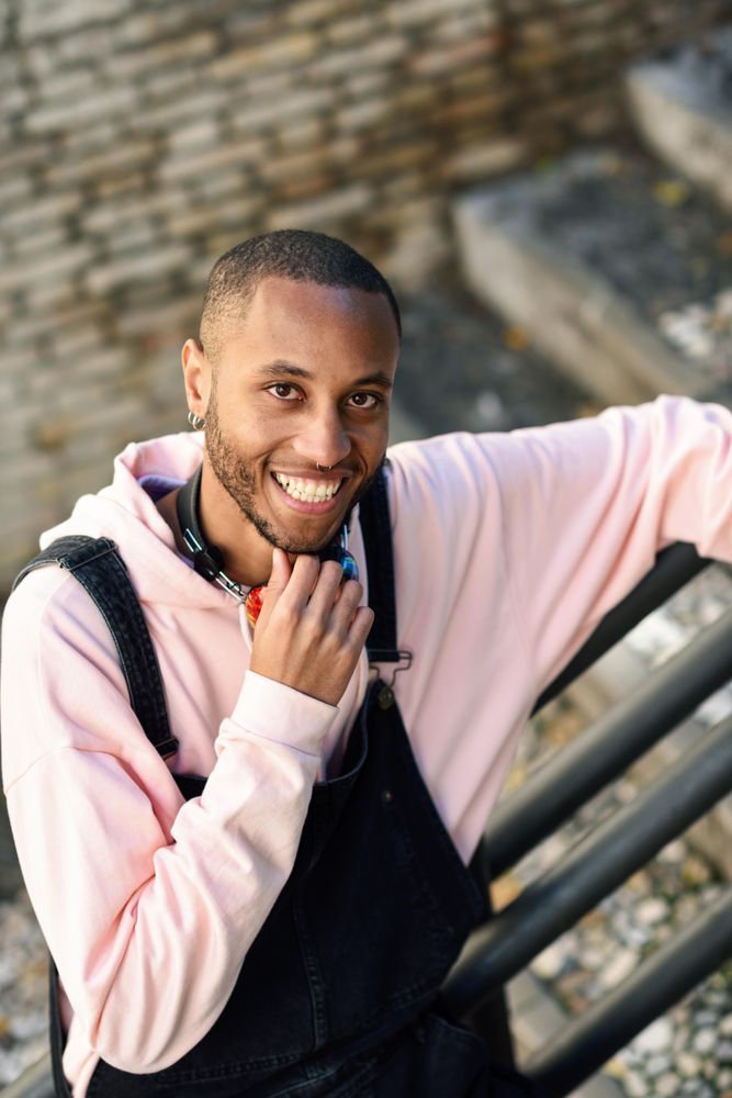Happy male in overalls and hoodie leaning on railing of stairs outside, vertical