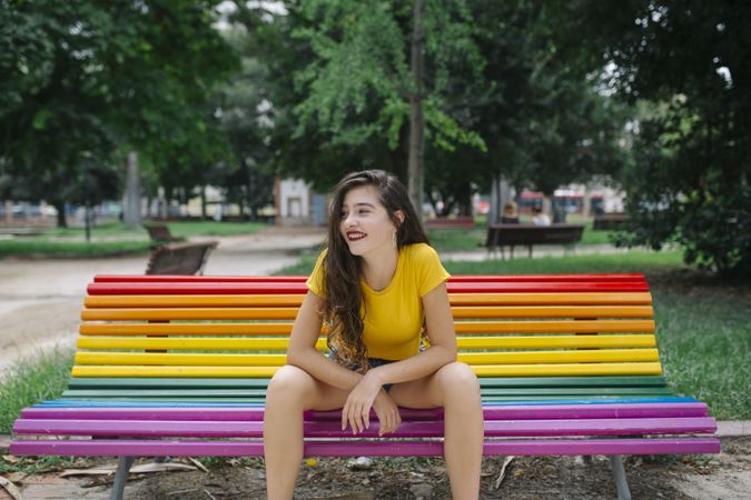 Cheerful woman sitting on rainbow bench