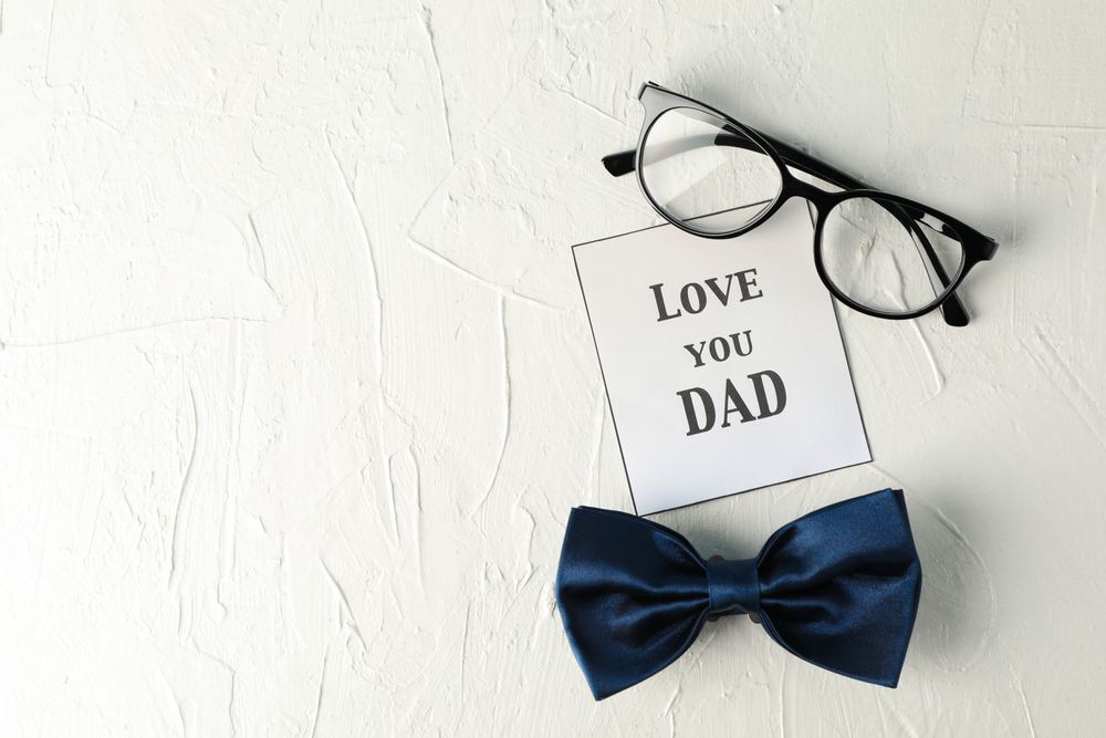 Inscription love you DAD, blue bow tie and glasses on plain background, space for text and top view