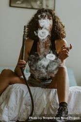 Woman sitting on bed smoking hookah bYkNg5