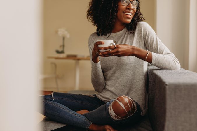 Smiling woman in fashionable torn jeans holding a coffee cup relaxing at home