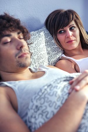 Angry woman looking at man sleeping next to her