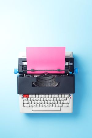 Typewriter with pink paper over blue background