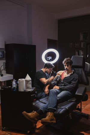 Master doing tattoo on forearm of male customer