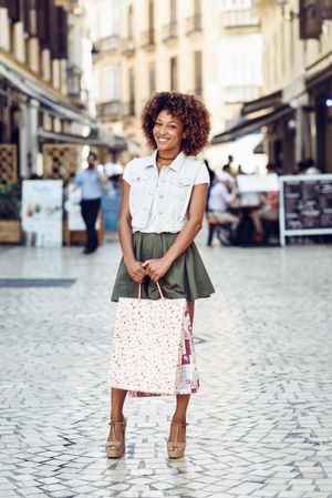 Smiling stylish woman on cobbled street with shopping bags