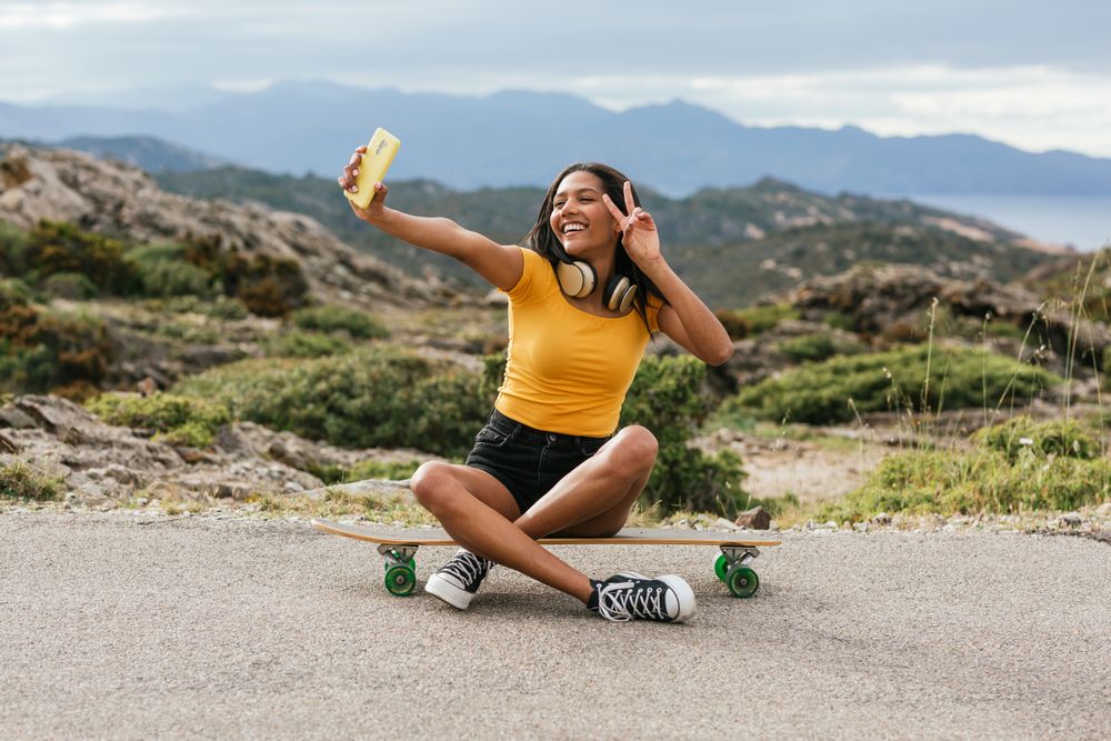 Delightful woman on longboard taking selfie on smartphone