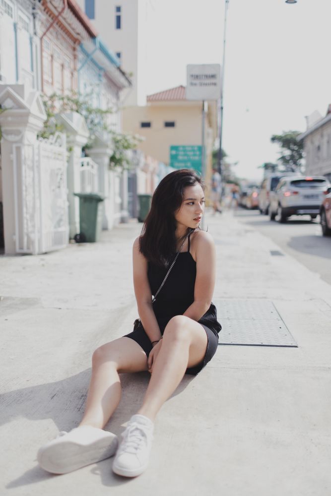 Woman in dark dress sitting on sidewalk during daytime
