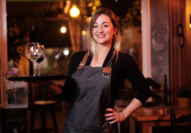 Cheerful waitress holding tray with wineglasses