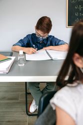 Boy with face mask writing at school