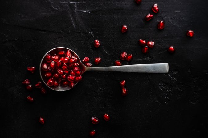 Spoon with pomegranate seeds on dark table