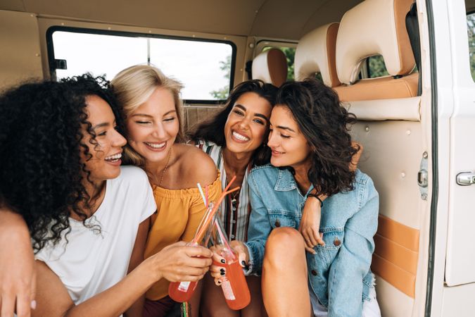 Two smiling women toasting with bottles in van