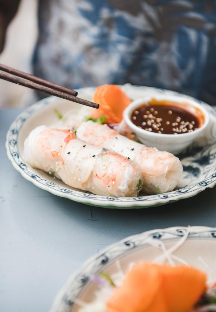 Chopsticks held above spring rolls, with dipping sauce