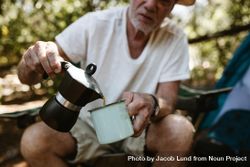Close-up of a older man pouring coffee in a mug at campsite. 5Rp1Nb