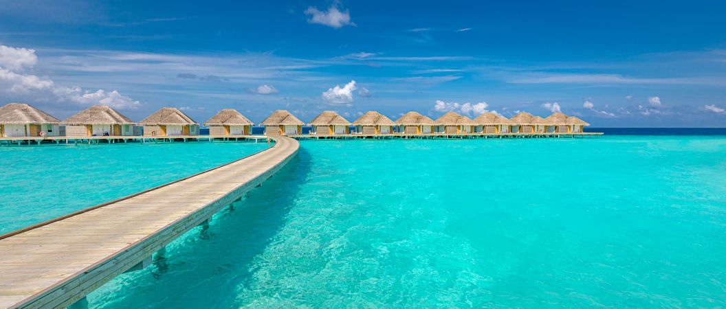 Wide shot of walkway on crystal clear tropical water with overwater bungalows