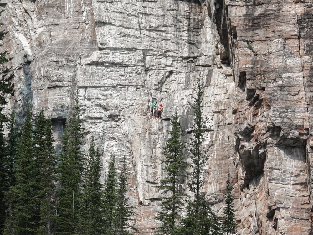 Two climbers on a ledge scaling a rock face next to Lake Louise