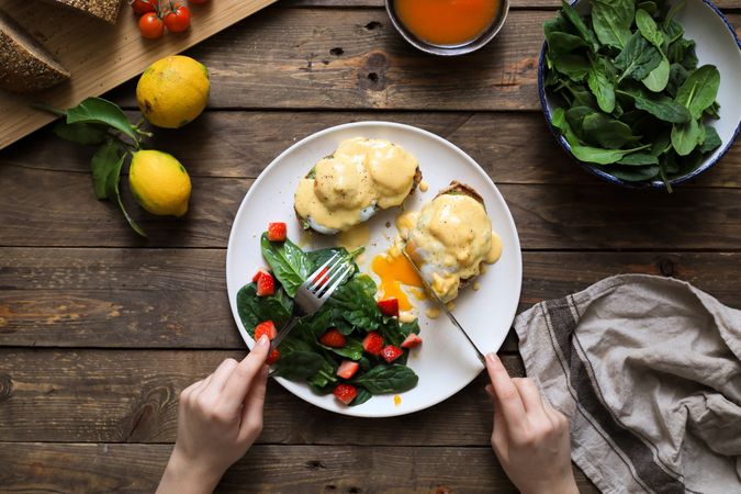 Person eating scrambled eggs on bread with green sauce and tomato