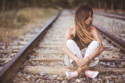 Long haired woman sitting on railways overgrown with dry grass