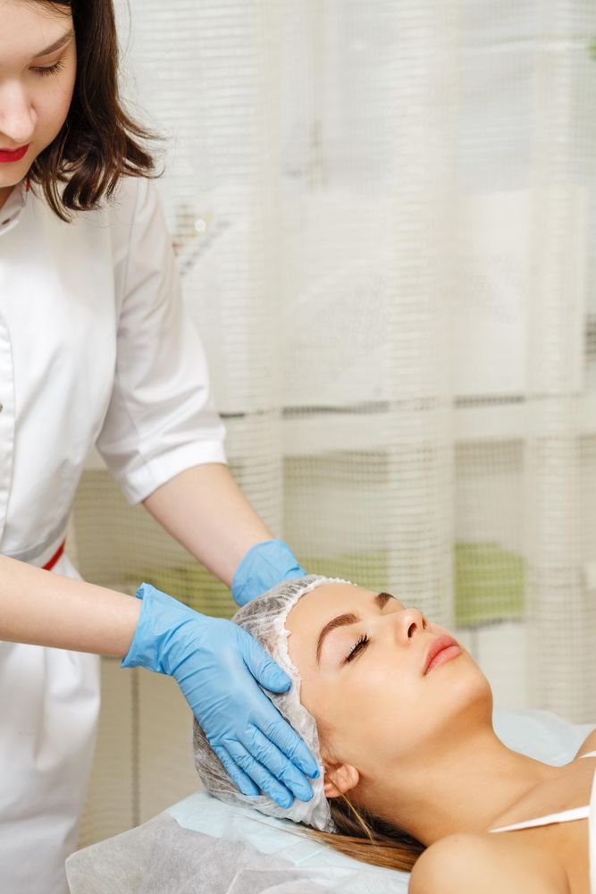 Female beautician preparing woman’s face and hair before facial