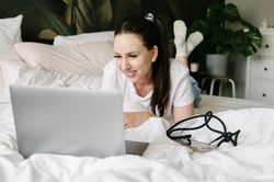 Smiling woman using laptop in bed during weekend