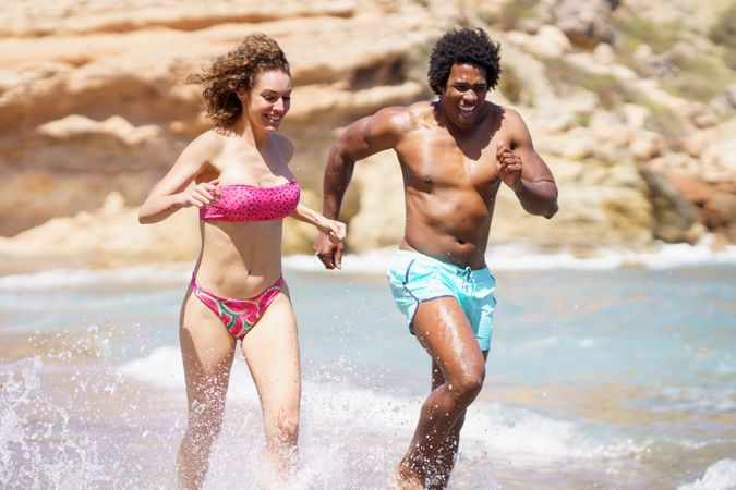 Black man and white woman running playfully along the coast