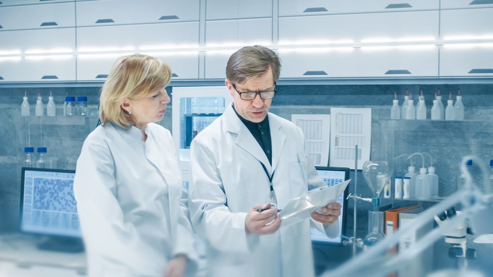 Female and Male Chief Scientists Walking Through Modern Laboratory and Discussing Future Possibilities.