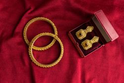 Beautiful shiny golden bangles and diamond studded traditional earrings on a red velvet background