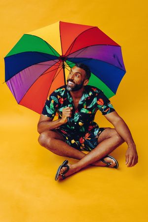 Happy Black male smiling  while sitting under colorful umbrella