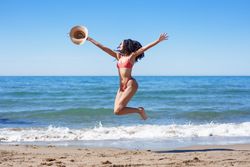 Joyful Summer Moments A Woman Joyfully Leaping on the Beach Wearing a Straw Hat
