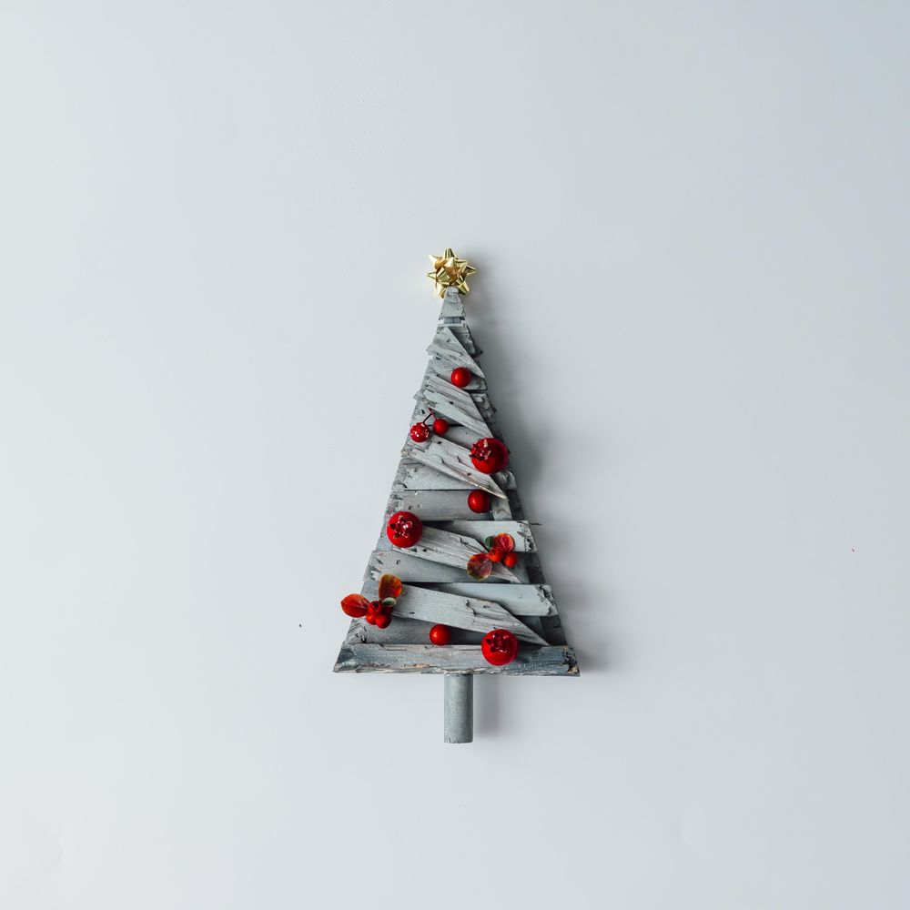 Decorative star topped wooden Christmas tree with red baubles on light background