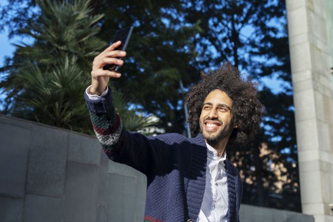 Smiling Black man taking selfie with smartphone while outside in the sun