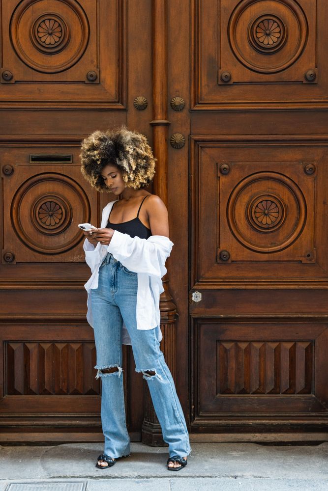 Serious Black woman browsing smartphone near old wooden door